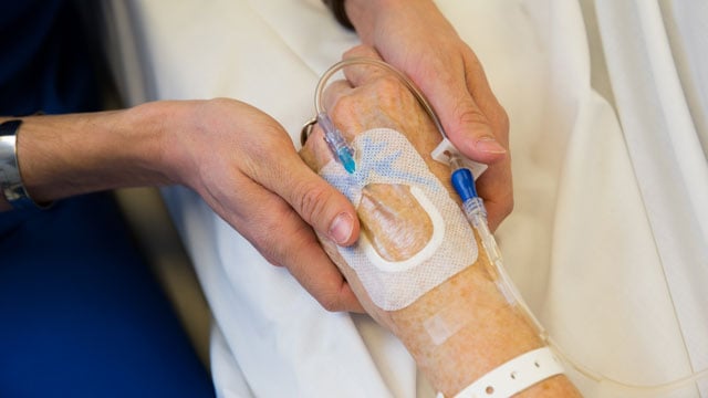 patient's hand with IV being held by nurses' hands