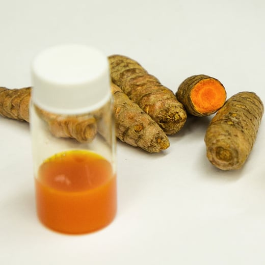 Vile with curcum formulation in front of tumeric roots