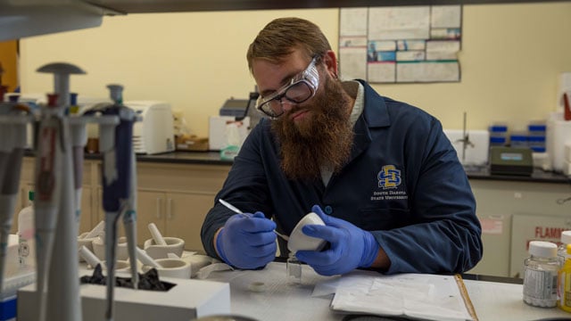 Doctoral student Kyle Burch puts crushed aspirin into a vial 