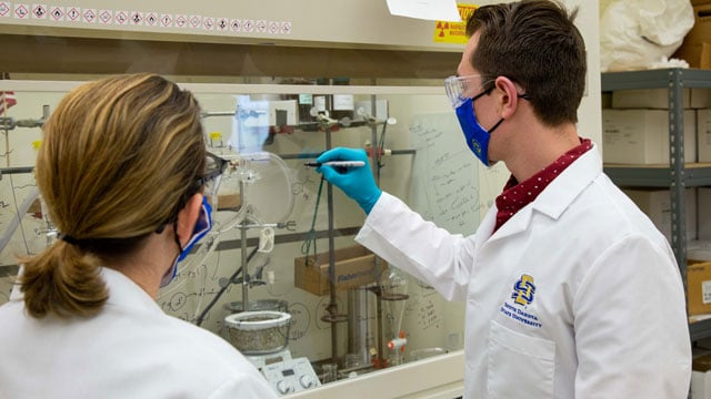 Willand-Charleny, left, with Paris writing equations on glass of the laboratory fume hood