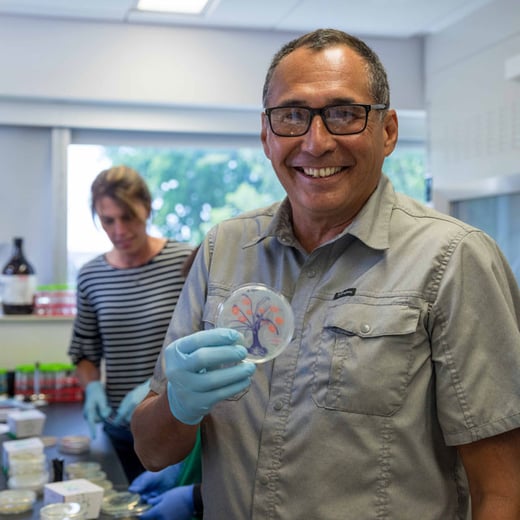 Teacher Brian LaBelle holds a petri dish with a tree he painted using bacteria