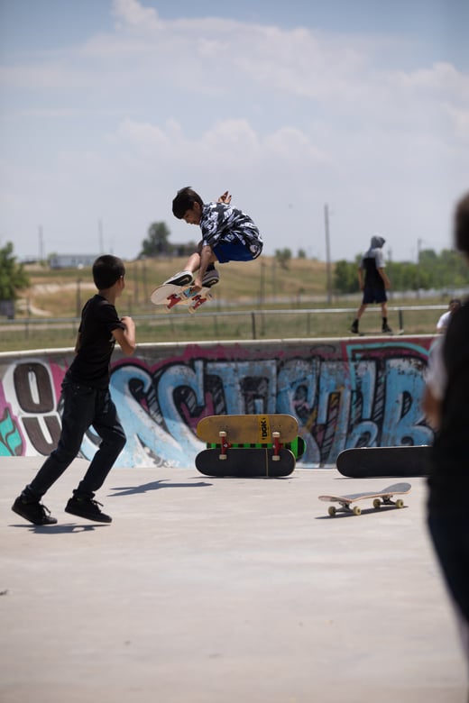 A Lakota boy is in mid-air on his skateboard jumping out of a bowl in a skate park and over a vertacle obstacle.
