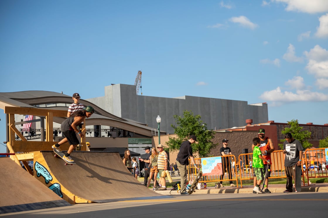 Pop-up skateboard park on Philips Ave in Sioux Falls. One of the skaters takes the half pipe while others watch.