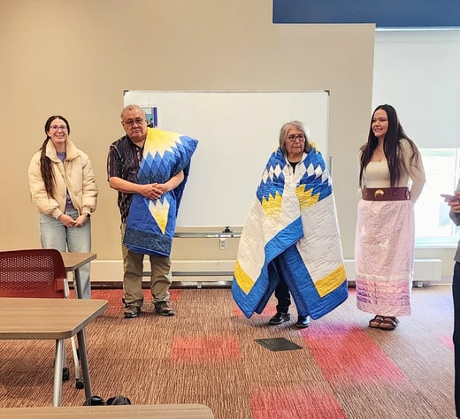 Two students pictured standing next to the two Lakota elders in residence for their honoring ceremony