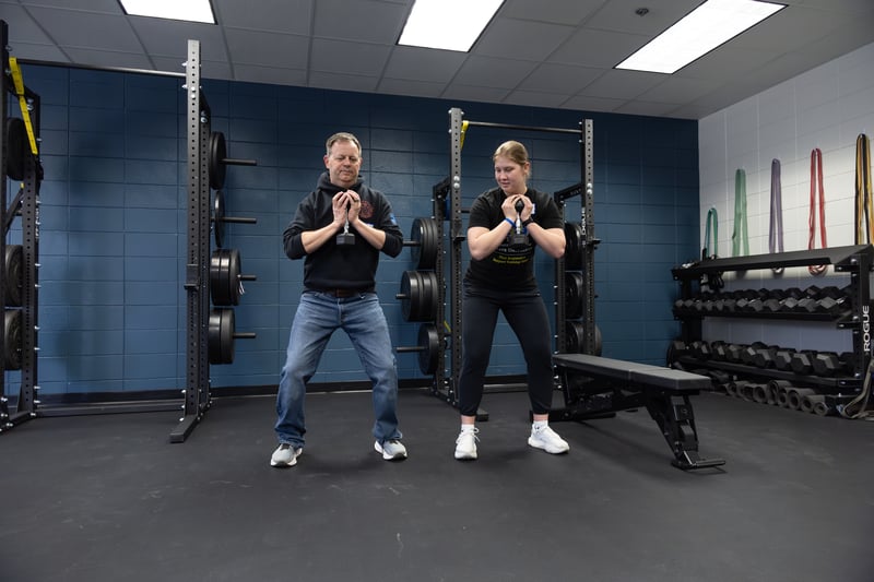 A firefighter and strength team member working on proper squatting form during the strength session of the Wellness Summit.