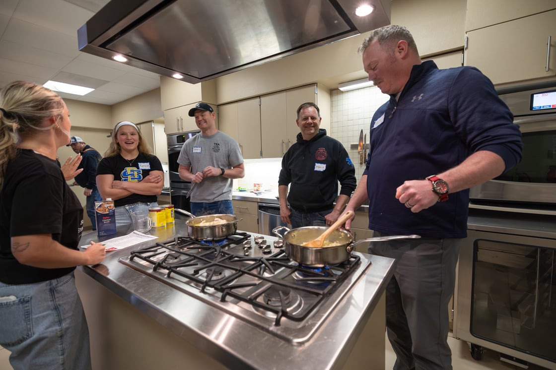 A group of firefighters cook in the kitchen while nutrition students assist