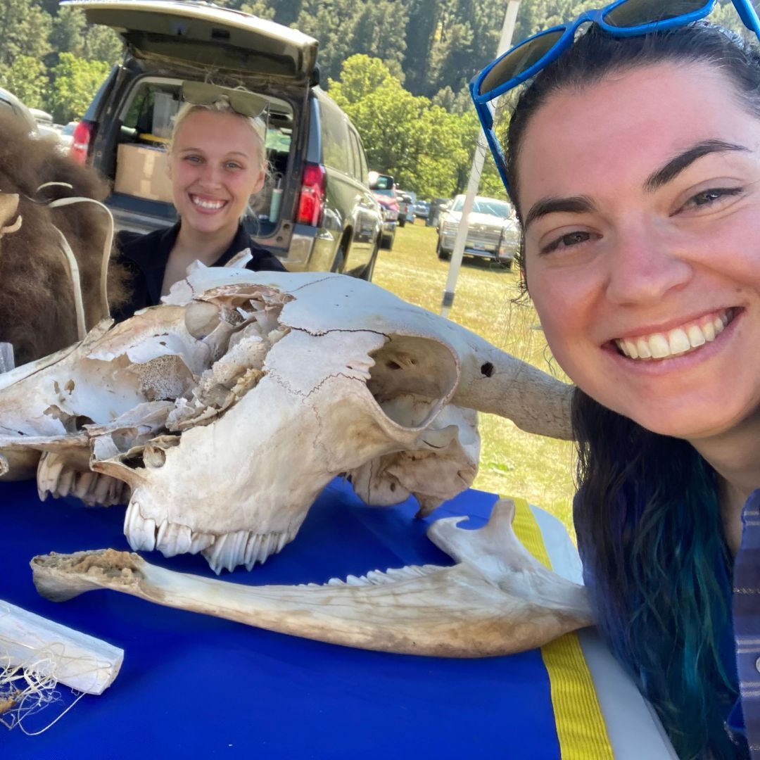 Two female students posing in the booth with bison skull and bones