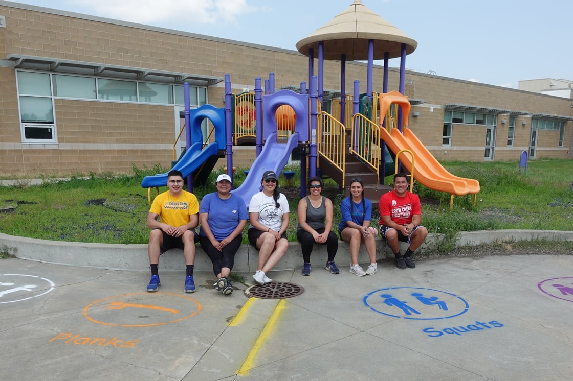 Group photo of participants sitting in front of playground set after they painted the playground floor with various stenciled images.