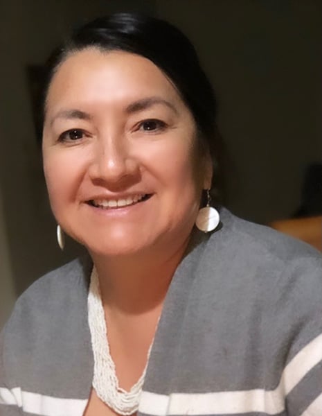 Dr. Dawn-Frank, Oglala Lakota woman smiles at the camera in a head-and-shoulders picture. She wears white jewelry and a white and grey cardigan..