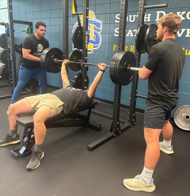 A research participant is pictured doing their bench press for the strength assessment and research assistants are spotting their lift.