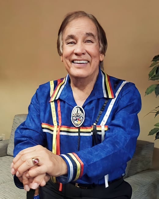 Billy Mills headshot wearing a ribbon shirt and sitting in a chair