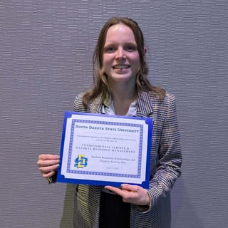 Katherine Pfeifle holds a blue-bordered certificate from South Dakota State University recognizing top poster work in Environmental Science and Natural Resource Management.