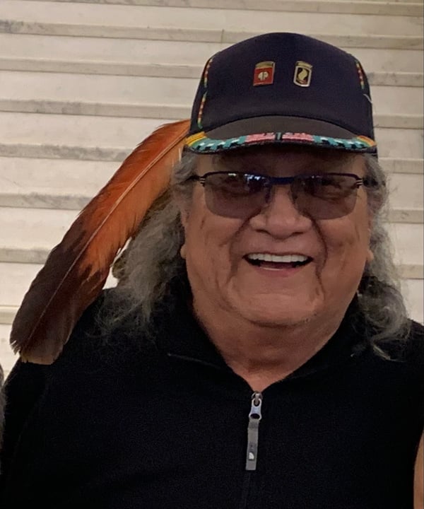 tom bad heart bull posing for a picture wearing a beaded black cap with veteran buttons and an eagle feather