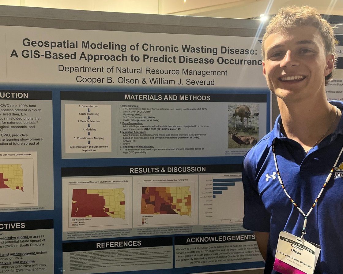 Cooper Olson is posing in front of his research poster