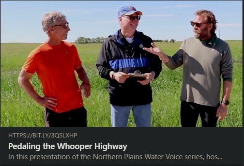 Three people standing in a green field during an outdoor interview or discussion, featured in a video titled “Pedaling the Whooper Highway” from the Northern Plains Water Voice series.