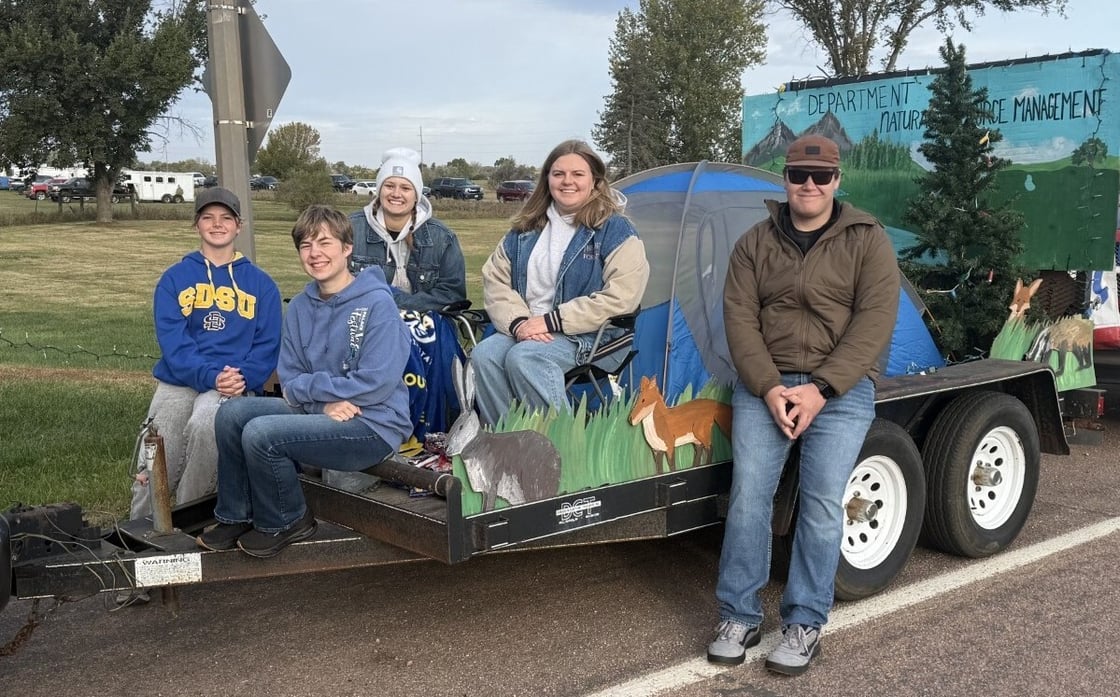 (from left to right: Ashlyn Sorensen, Dakota Fuerst, Izzy Tronnes, Amara Roland and Kaden Ball) Five students are posing on the trailer they decorated for the parade