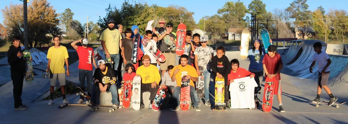 Group picture of Lakota skateboarders children and adults posing for the camera at the skate park with their skateboards.