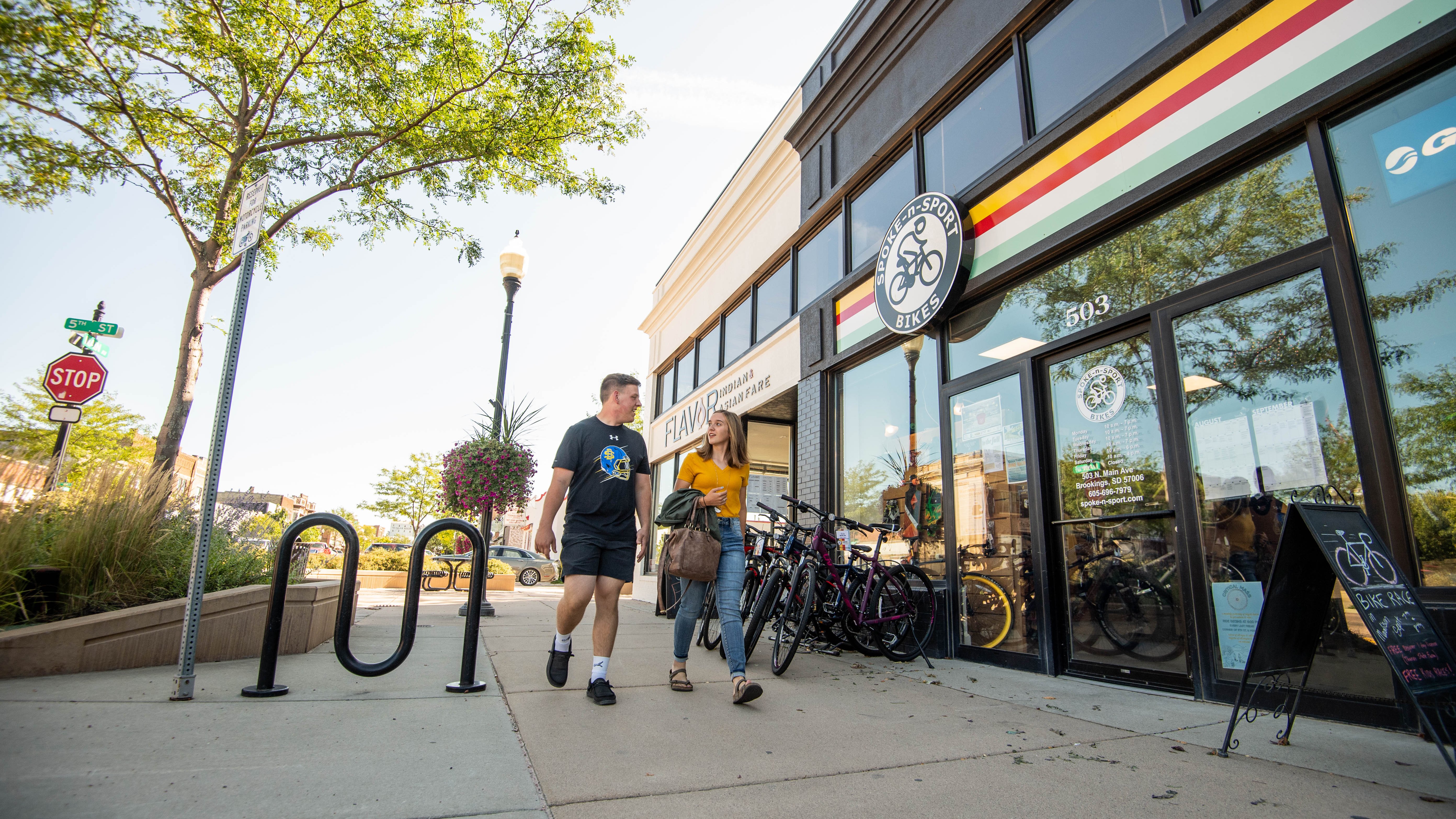 two students walking downtown Brookings outside of a restaurant and a bike shop